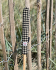 Mairead Hume® Black & White Houndstooth Harris Tweed® Golf Alignment Stick Cover — outdoor lifestyle shot leaning against a natural fence