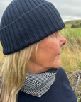 Person wearing a navy knit beanie and patterned scarf outdoors with grass and sky in the background