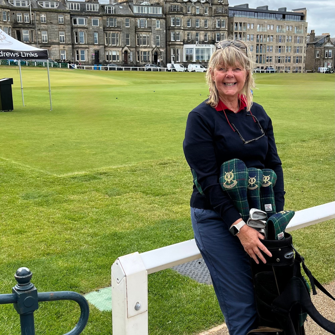 Woman holding golf clubs on a golf course with st andrews in the background