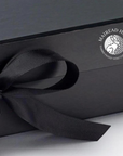 A black gift box with a bow on top, featuring a white logo and text on the lid.