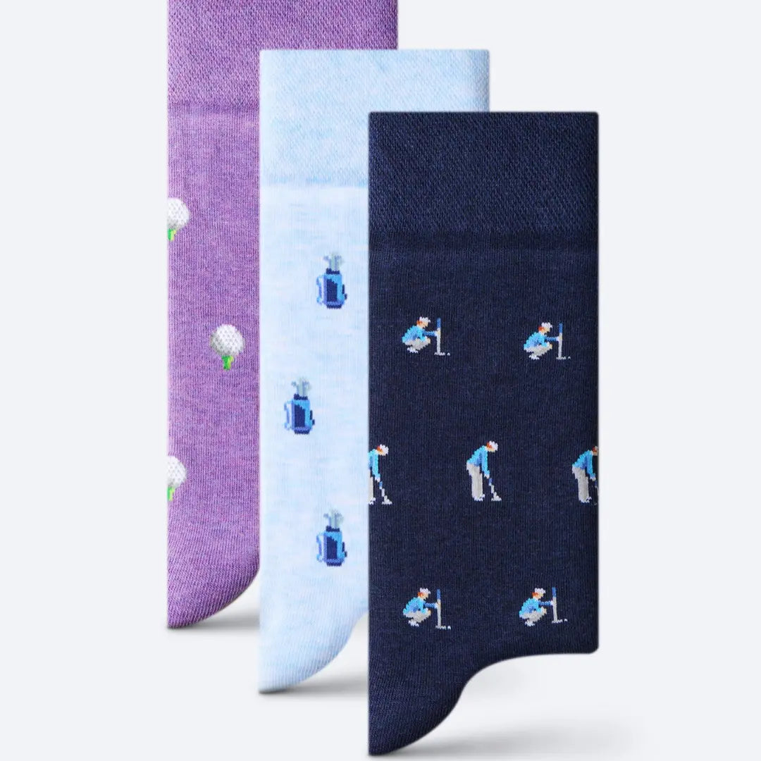 Three pairs of patterned socks displayed in a vertical stack on a light gray background. The front pair is dark navy blue with a repeating golf club and ball player motif, the middle pair is light blue with blue and white golf ball and club motifs, and the back pair is purple with white golf ball and green stem motifs.