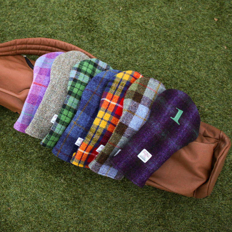 Set of colorful plaid golf head covers on a brown bag against a green grass background