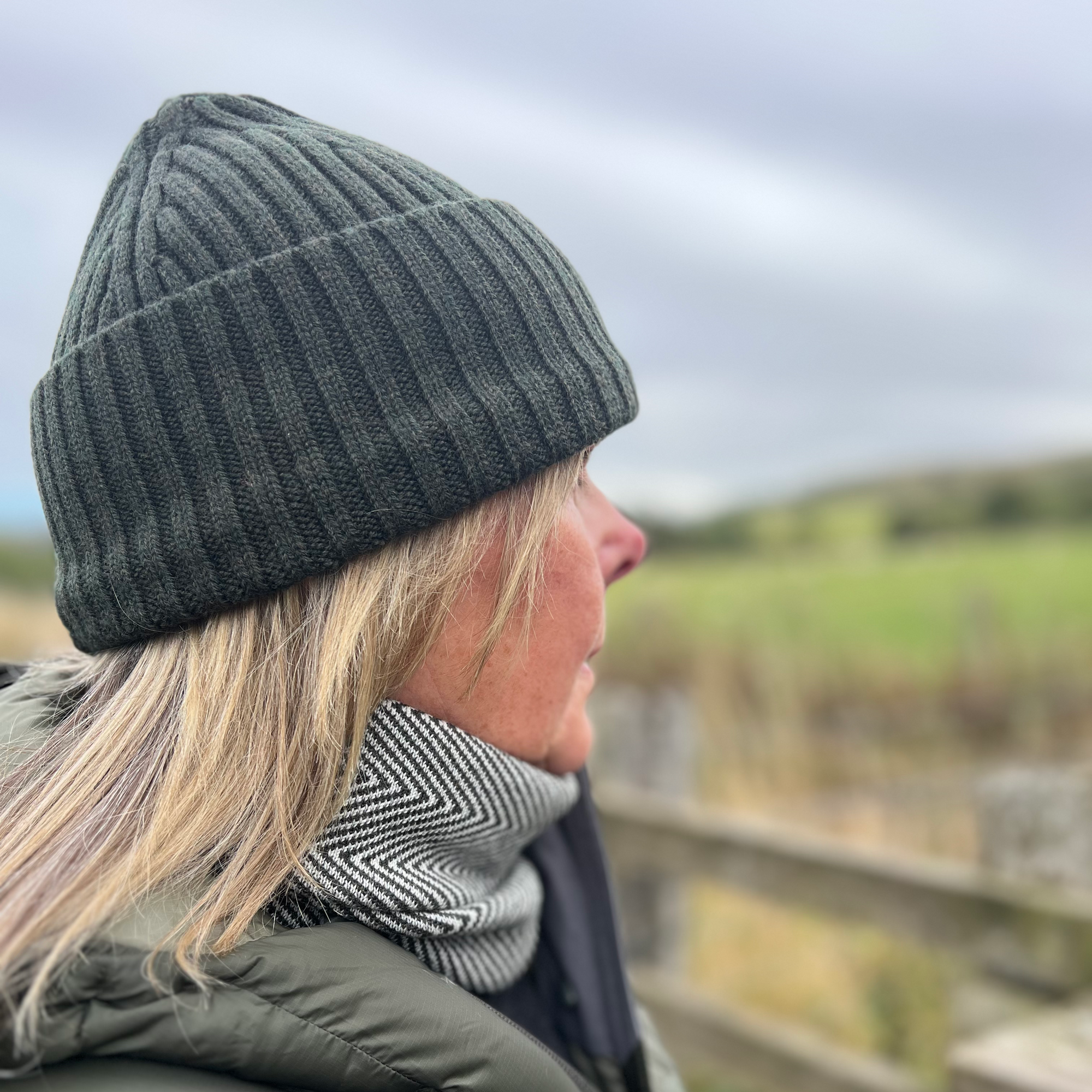 Person wearing a gray beanie and scarf with a scenic background